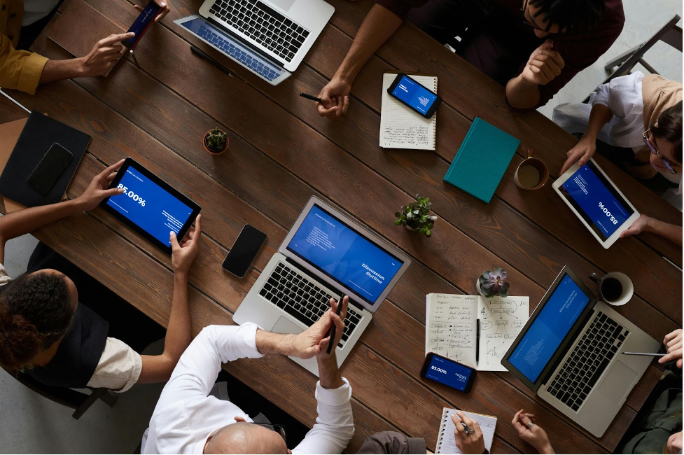 Grupo de personas en una mesa de madera utilizando diversos dispositivos para acceder a software de gestión, vista aérea