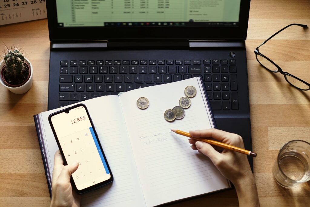 Persona calculando CUCA en libreta con monedas y laptop para gestión contable