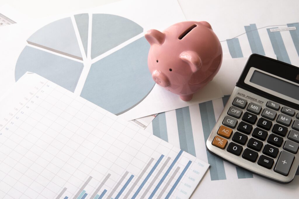 Elementos visuales relacionados con un fondo de ahorro empresa: alcancía rosa, calculadora y gráficos financieros sobre una mesa