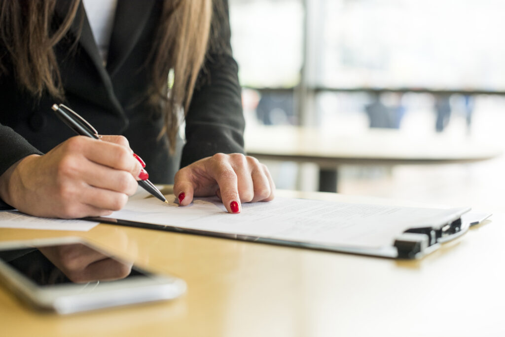 Mujer firmando documento en oficina, relacionado con trámites fiscales y constancia de situación fisca