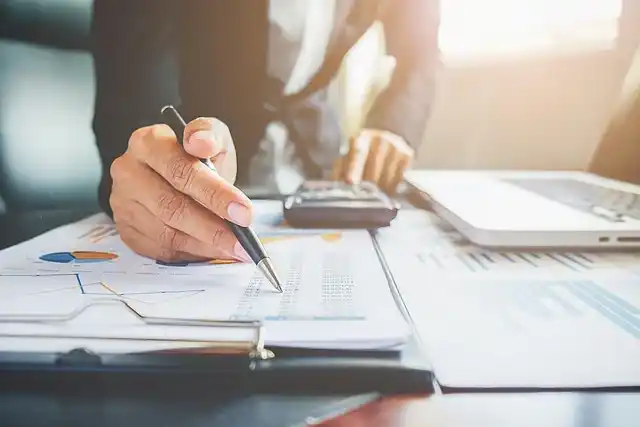 Mano revisando reportes financieros con calculadora y laptop en escritorio de oficina