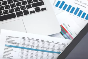 Documentos contables con tablas financieras y gráficos junto a una computadora portátil, usados para análisis y control financiero